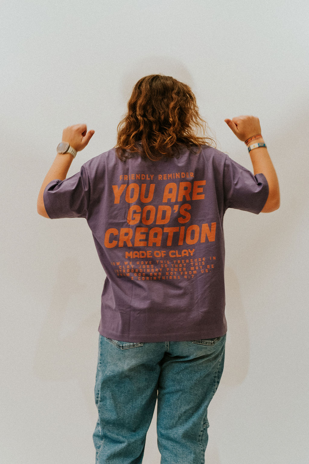 The back of a Made of Clay t-shirt printed with “Friendly reminder: you are God’s creation” and 2 Corinthians 4:7